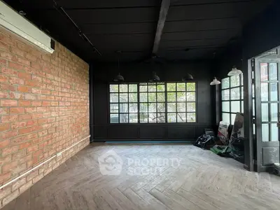 Spacious industrial-style room with brick wall and large windows, perfect for creative workspace or studio.