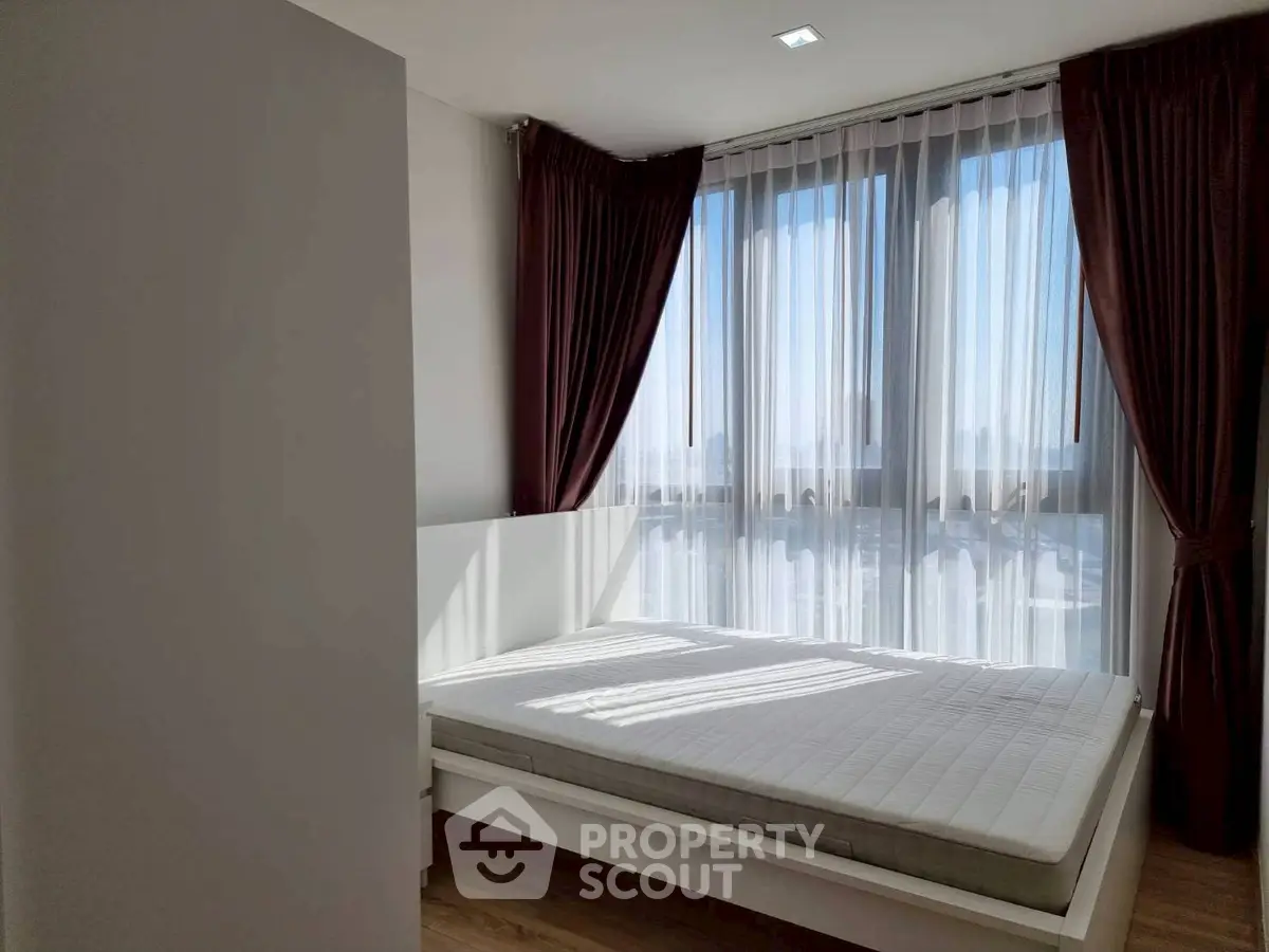 Modern bedroom with large windows and elegant curtains, featuring a minimalist bed frame and natural light.