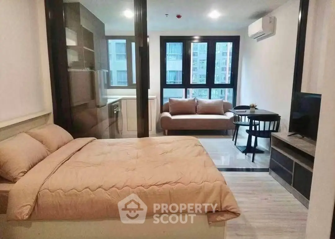 Modern studio apartment with cozy bed, stylish sofa, and sleek kitchen area.