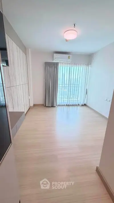 Spacious empty living room with large window and wooden flooring in modern apartment.