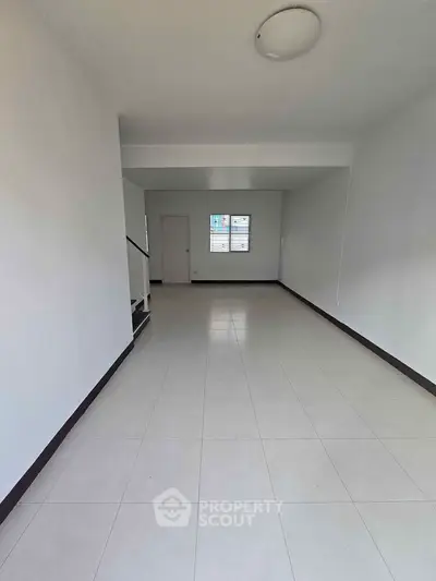 Spacious empty room with tiled flooring and staircase, ideal for customization.