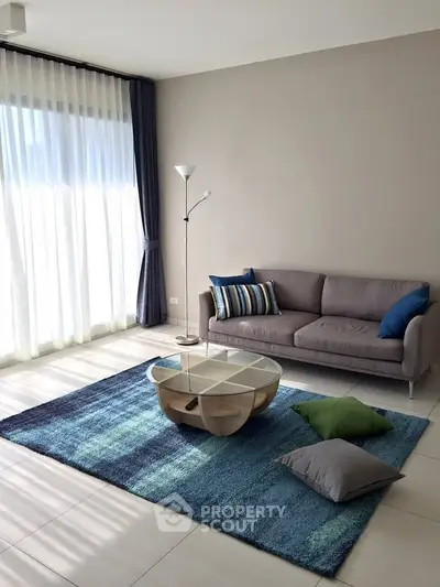 Modern living room with stylish sofa, vibrant rug, and floor-to-ceiling windows for natural light.