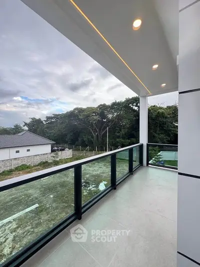 Spacious balcony with modern glass railing and scenic view of lush greenery, perfect for relaxation.