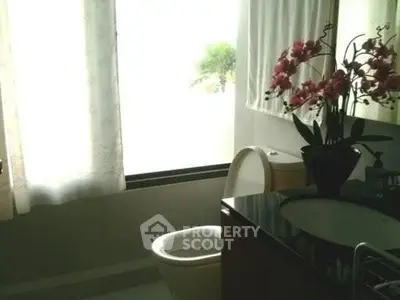 Elegant bathroom with large window and floral decor, offering a serene and bright atmosphere.