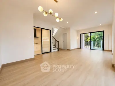 Spacious open-plan living room with modern lighting and large windows overlooking greenery.