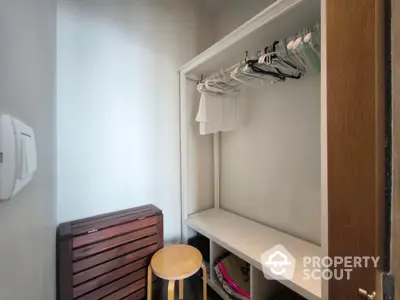 Compact storage space with hangers and wooden stool in modern apartment.