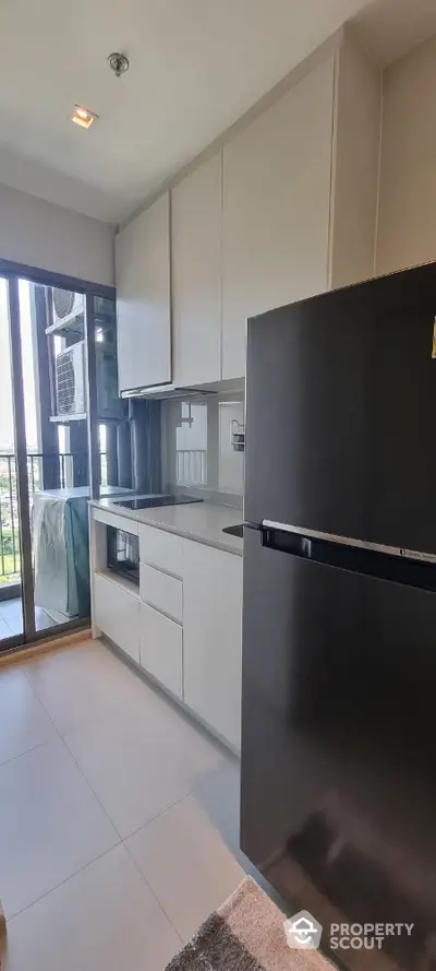 Modern kitchen with sleek cabinets and large fridge, featuring balcony view.