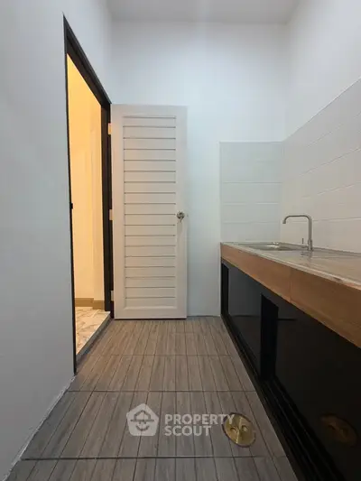 Modern kitchen with sleek wooden cabinetry and tiled flooring, featuring a minimalist design and ample natural light.
