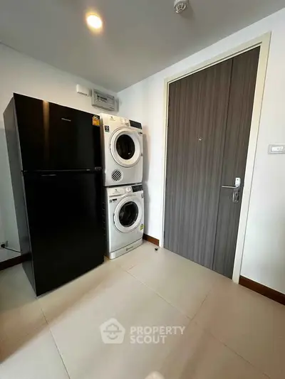 Modern laundry area with stacked washer and dryer next to sleek refrigerator.