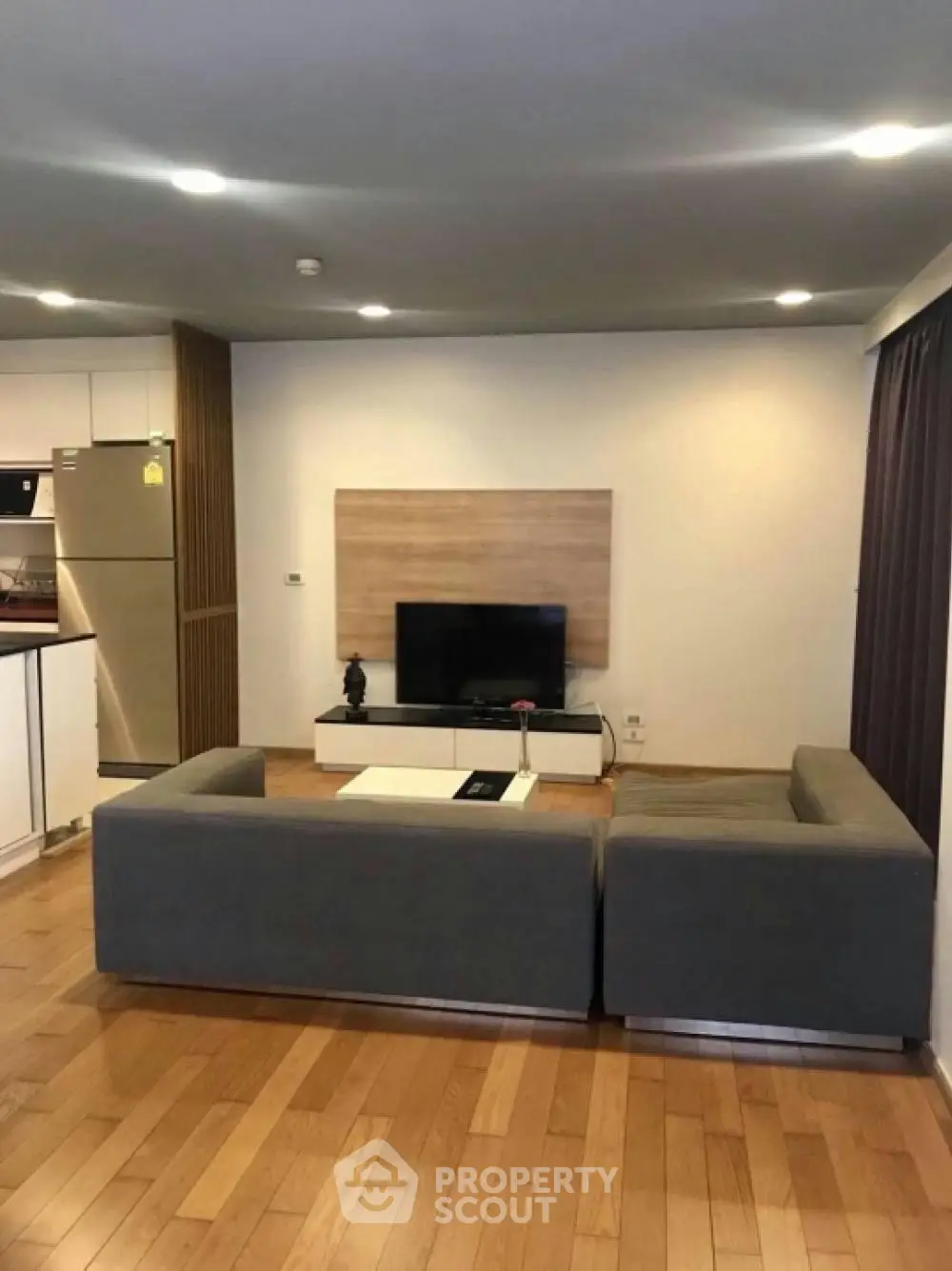 Modern living room with sleek furniture and open kitchen layout, featuring a stylish TV setup and wooden flooring.