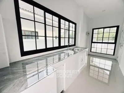 Sleek modern kitchen with large windows and marble countertops in a bright, airy space.