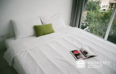 Cozy bedroom with large window and lush green view, featuring a neatly made bed with white linens and a green pillow.