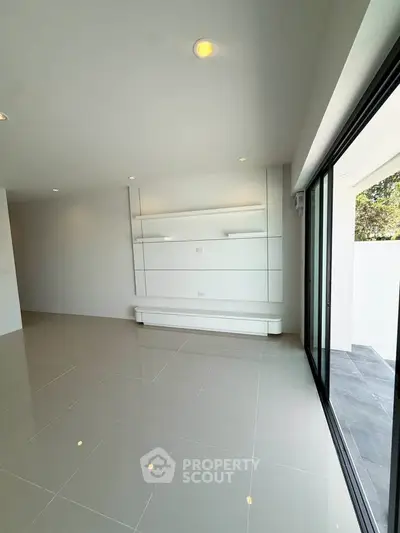 Spacious modern living room with sleek tile flooring and large sliding glass doors opening to a balcony.