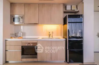 Modern kitchen with sleek wooden cabinets, built-in oven, microwave, and black refrigerator.