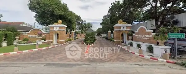 Grand entrance of a luxurious residential complex with lush greenery and elegant architecture.