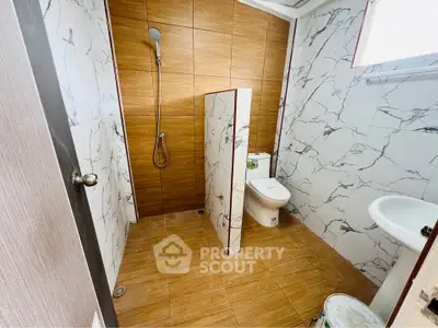 Modern bathroom with marble tiles and wooden accents, featuring a sleek shower and contemporary fixtures.