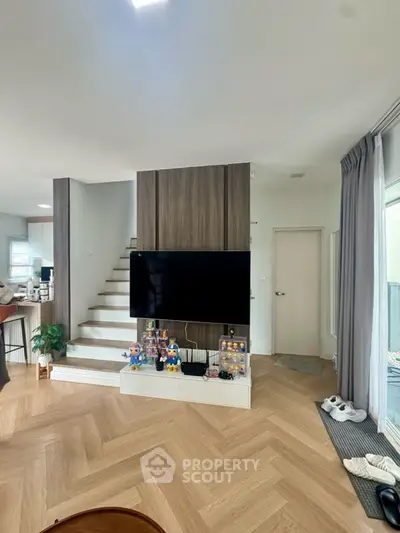 Modern living room with stylish wood flooring and large TV, open layout design.