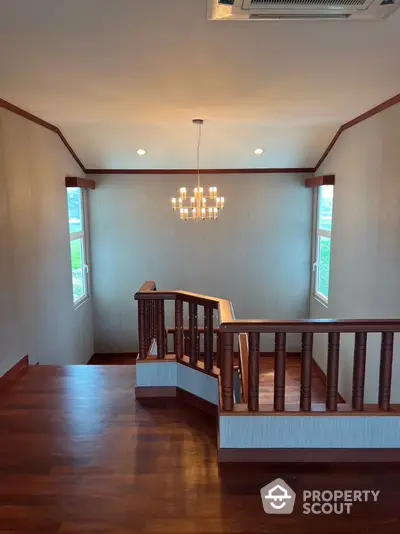 Elegant staircase with wooden railing and modern chandelier in a spacious hallway