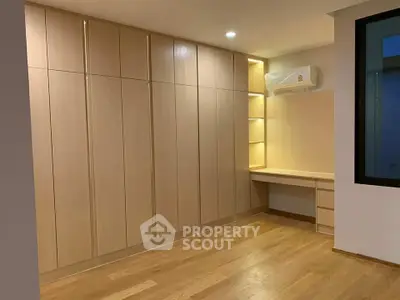 Spacious room with built-in wooden wardrobe and desk, featuring modern lighting and hardwood floors.