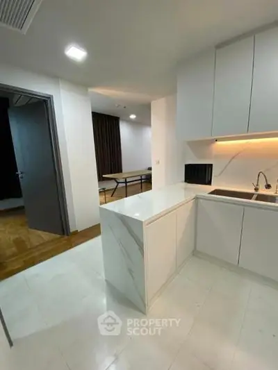 Modern kitchen with sleek white cabinetry and marble countertops in open layout apartment.