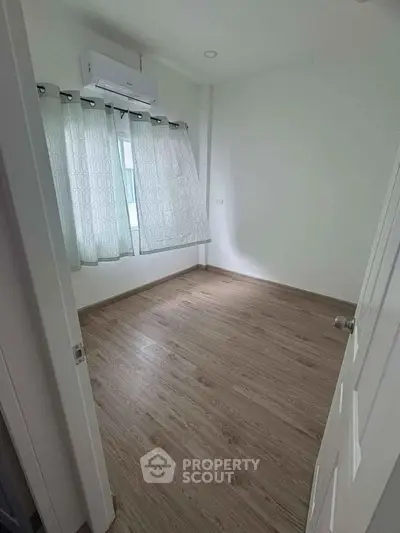 Spacious empty bedroom with wooden flooring and air conditioning unit.