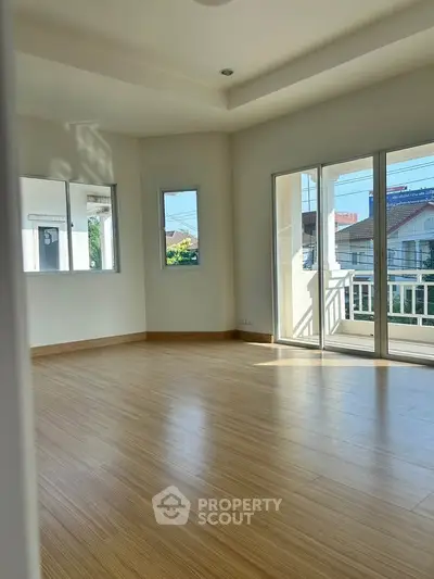 Spacious sunlit room with wooden flooring and large windows in a modern home.