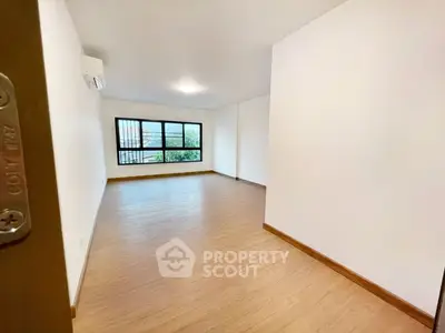 Spacious empty room with wooden flooring and large window view.