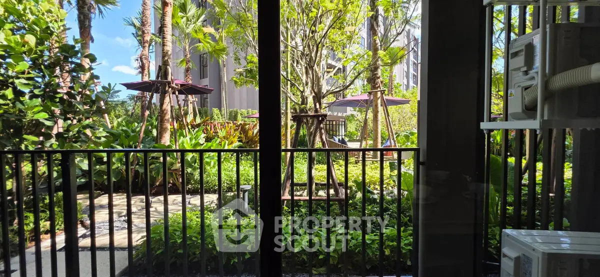 Lush garden view from a modern apartment balcony with vibrant greenery and outdoor seating.