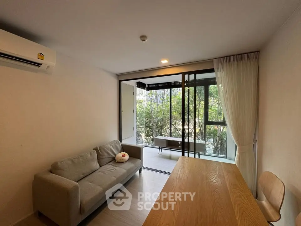Modern living room with cozy sofa and large window opening to a lush balcony view.