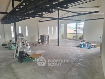 Spacious industrial-style loft under renovation with large windows and concrete flooring.