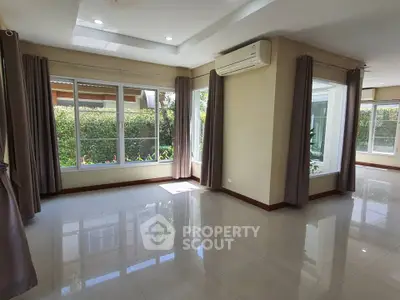 Spacious living room with large windows and garden view, featuring modern air conditioning and elegant curtains.