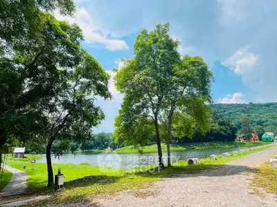 Scenic view of lush green landscape with trees and a serene lake under a bright blue sky.
