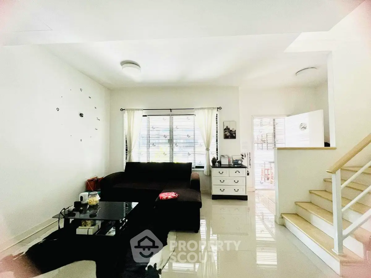 Modern living room with sleek black sofa and glass coffee table, bright natural light and minimalist decor.