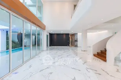 Luxurious modern interior with marble flooring and pool view, featuring elegant staircase and expansive windows.