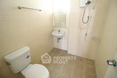 Compact bathroom with shower, sink, and toilet in a tiled setting.