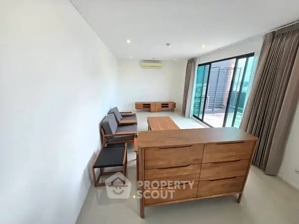 Spacious modern living room with wooden furniture and large windows offering natural light.