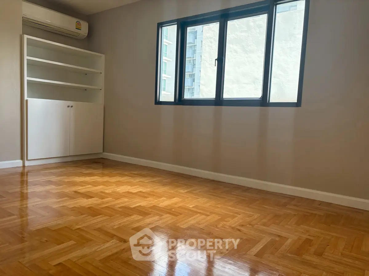 Spacious room with parquet flooring and built-in shelves, perfect for customization.