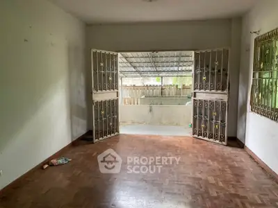 Spacious living room with open doors leading to a covered patio, featuring wooden flooring and metal security gates.