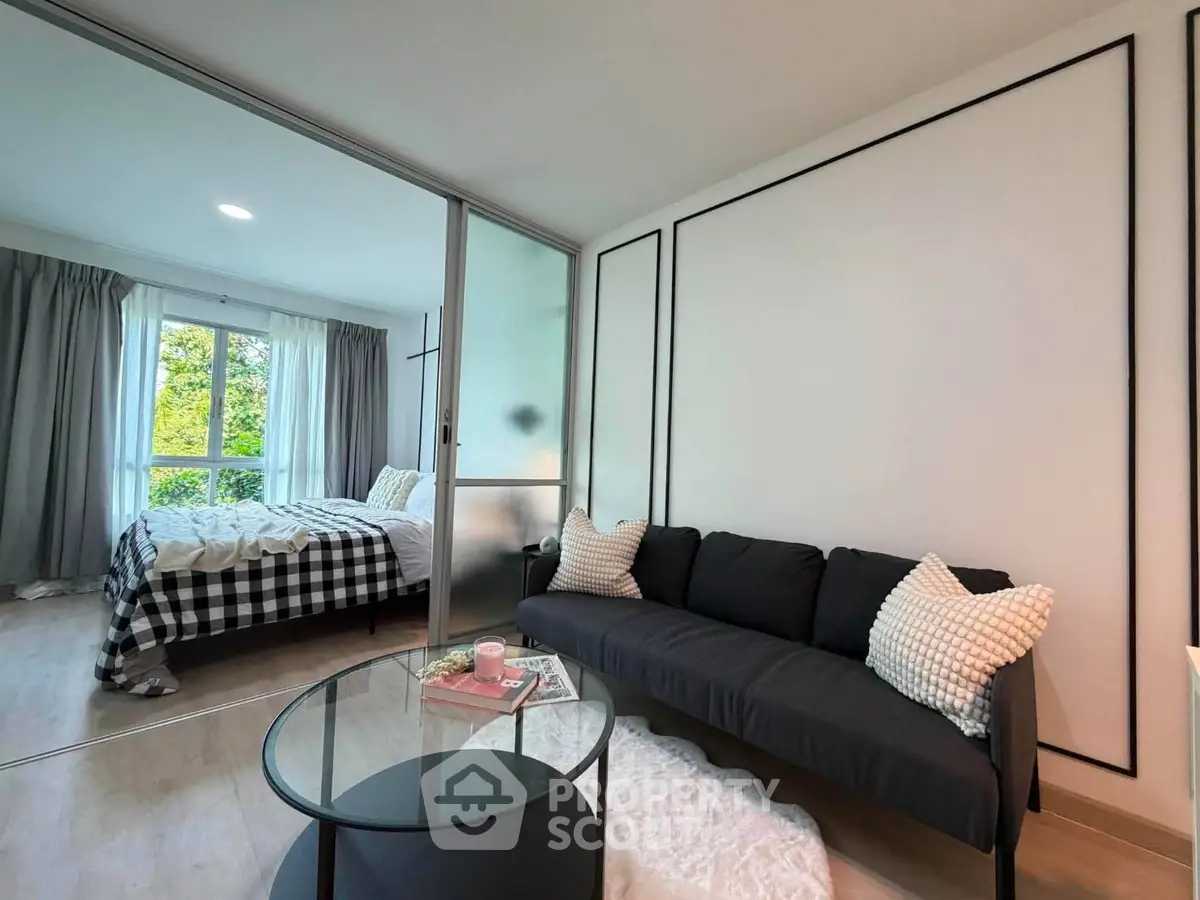 Modern living room with cozy sofa and stylish decor, adjacent to a bright bedroom with large windows.