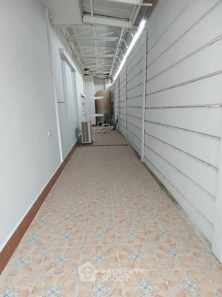 Spacious corridor with tiled flooring and covered ceiling, ideal for utility or storage use.