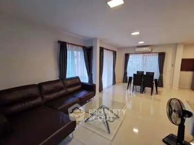 Spacious living room with modern furniture and dining area, featuring large windows and sleek design.