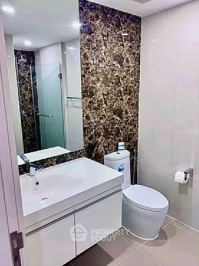 Modern bathroom with sleek design and marble accent wall, featuring a spacious vanity and glass shower enclosure.