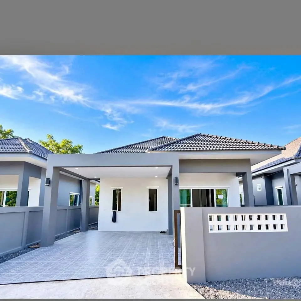 Modern single-story house with tiled roof and spacious driveway under clear blue sky.