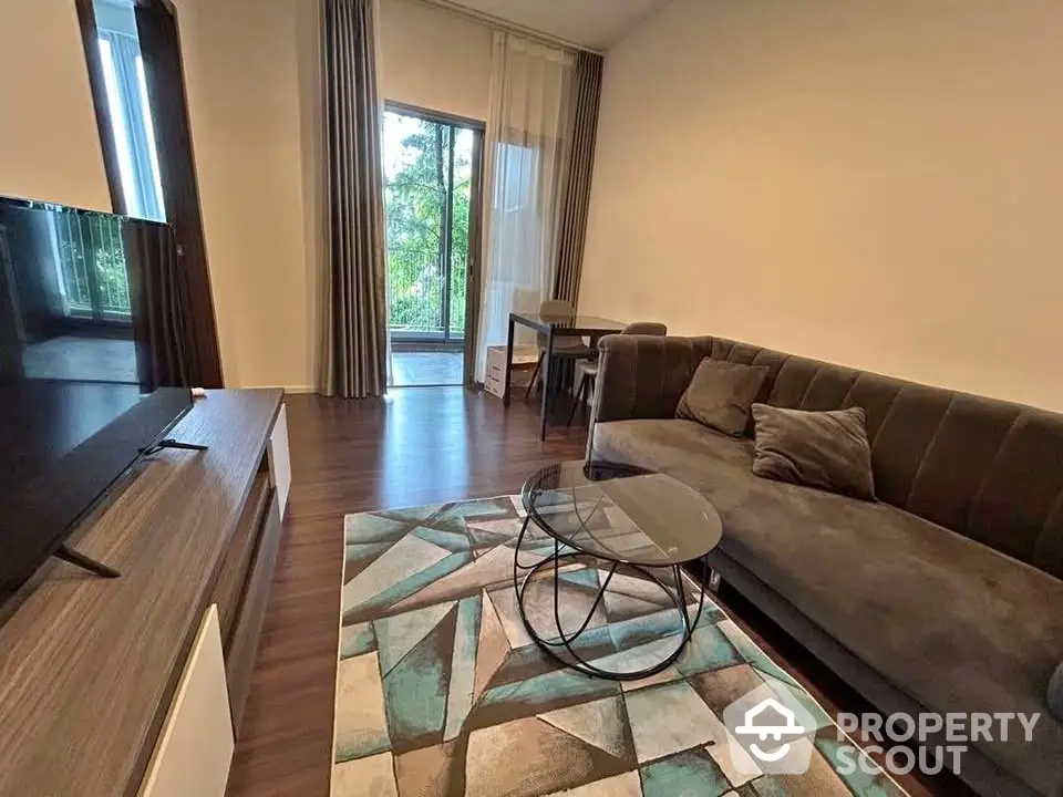 Modern living room with stylish sofa and glass coffee table, featuring a view of lush greenery through large windows.