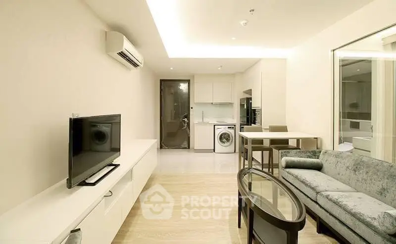 Modern living room with open kitchen, featuring sleek furniture and integrated appliances.