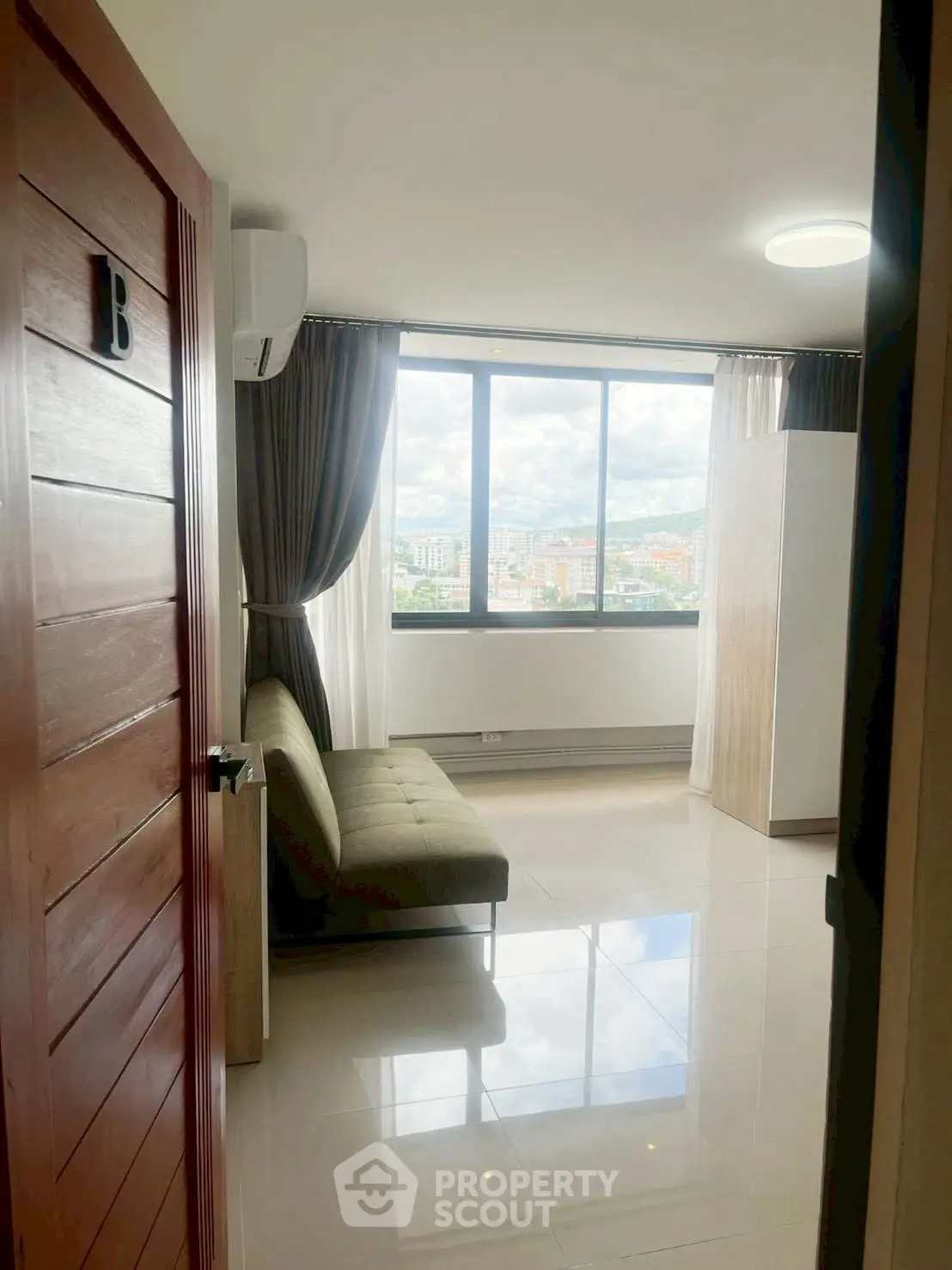 Bright living room with large window offering stunning city views, modern sofa, and sleek tiled flooring.