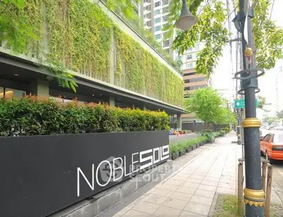 Modern building exterior with lush greenery and stylish signage on a city sidewalk.