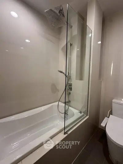 Modern bathroom with sleek bathtub and glass shower enclosure in a contemporary apartment.