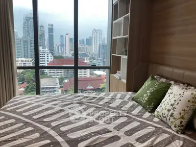 Modern bedroom with city view from large window, featuring stylish bedding and built-in shelving.