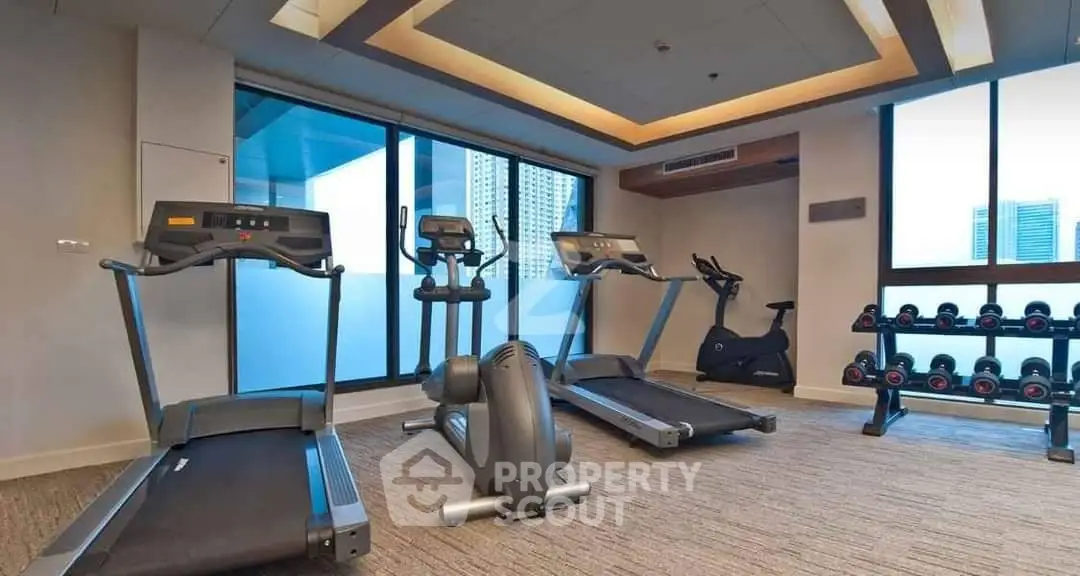 Modern gym with treadmills and weights in a high-rise building offering city views.